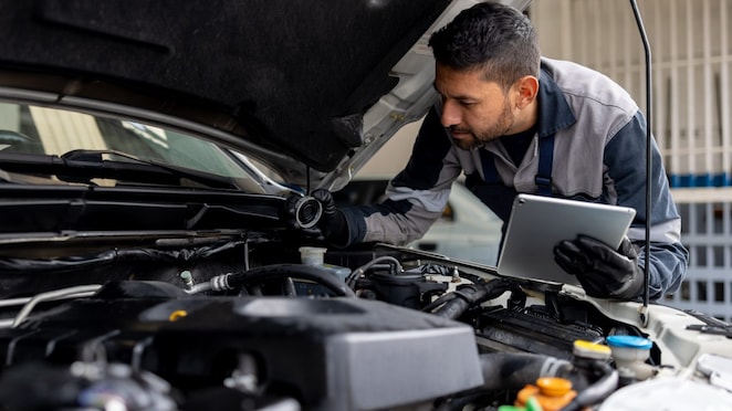 Male mechanic checking the levels of a liquid on a car using a tablet digital device in a garage auto repair shop.