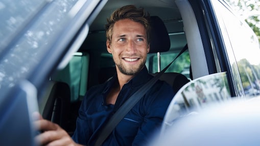 Uśmiechnięty mężczyzna siedzący za kierownicą samochodu osobowego