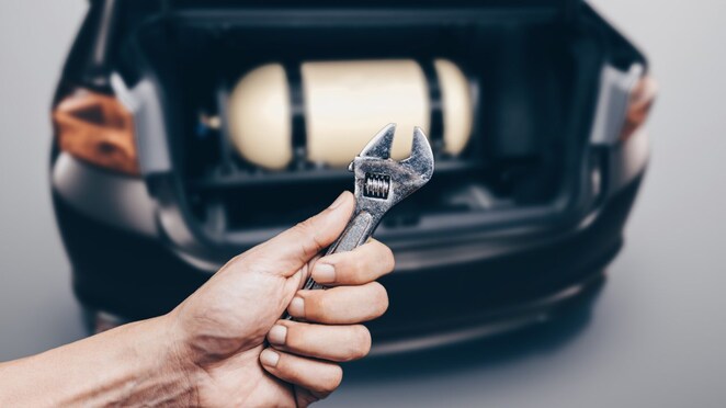 ręka z kluczem na tle butli gazowej w samochodzie