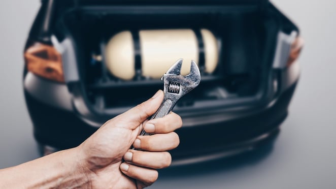 ręka z kluczem na tle butli gazowej w samochodzie