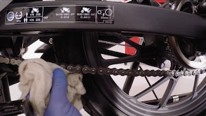 Ręka usuwająca nadmiar środka smarnego z łańcucha motocyklowego