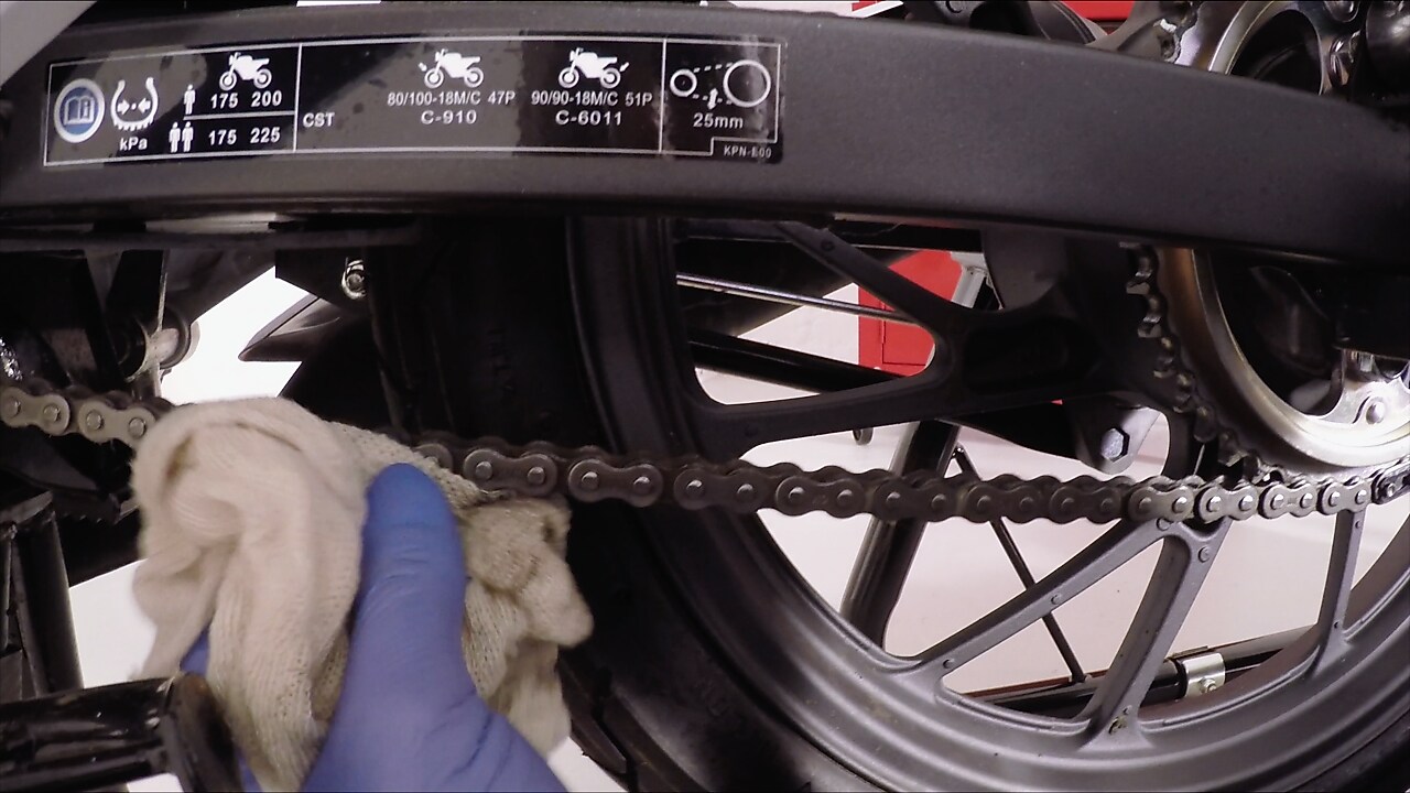 Ręka usuwająca nadmiar środka smarnego z łańcucha motocyklowego