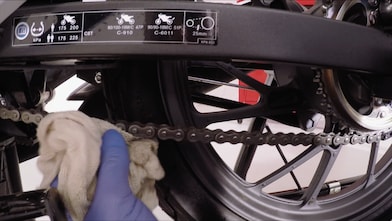 Ręka usuwająca nadmiar środka smarnego z łańcucha motocyklowego