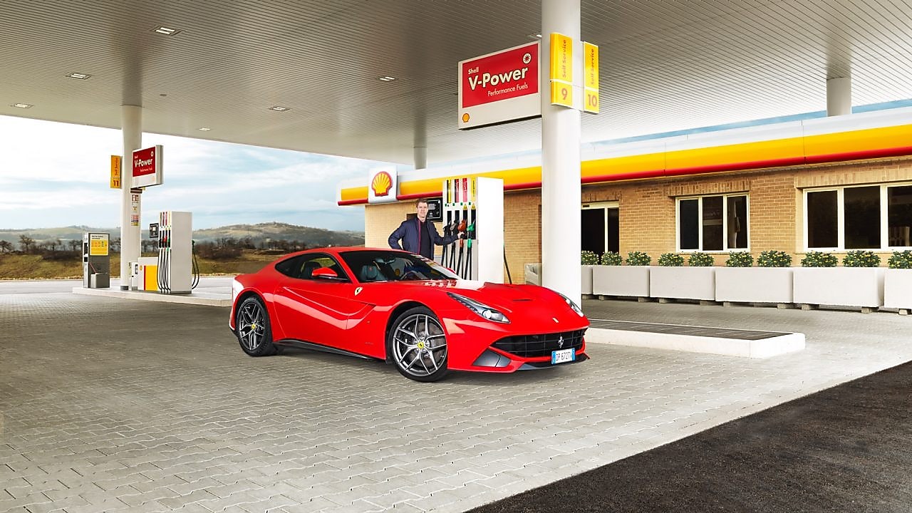 Czerwone Ferrari zaparkowane na podjeździe stacji Shell i mężczyzna sięgający do dystrybutora paliwa