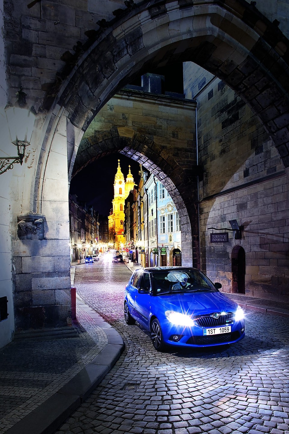 Niebieski samochód zaparkowany pod łukiem na brukowanej praskiej ulicy nocą