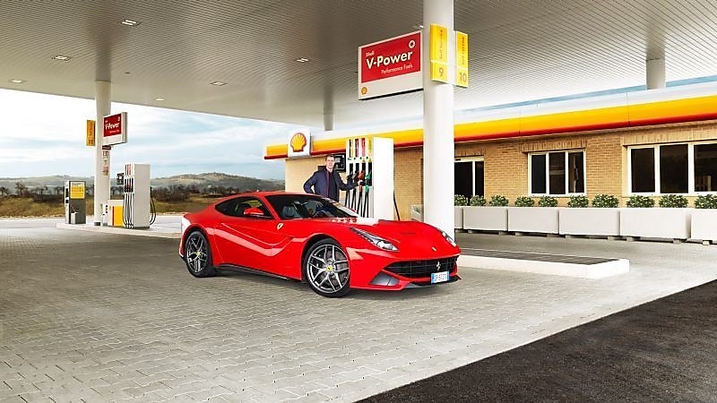 Czerwone Ferrari zaparkowane na podjeździe stacji Shell i mężczyzna sięgający do dystrybutora paliwa