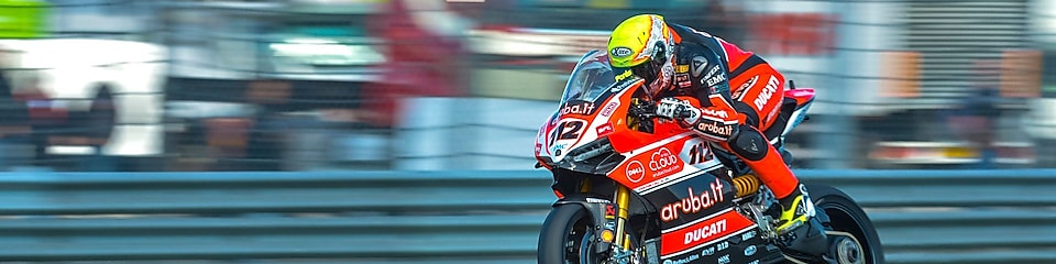 Superbike Ducati z zawodnikiem mknącym po torze wyścigowym, z ciężarówkami w tle