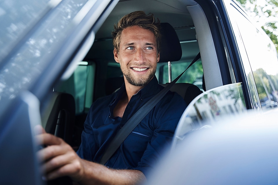 Uśmiechnięty mężczyzna siedzący za kierownicą samochodu osobowego