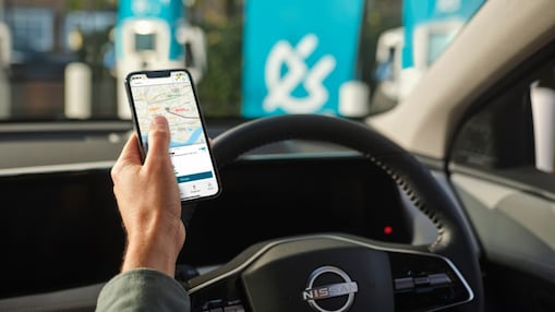 Osoba przy stacji ładowania dla pojazdów elektrycznych, patrząca na telefon