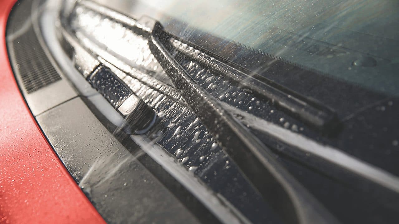 Zbliżenie na maskę czerwonego samochodu i jego przednią szybę.