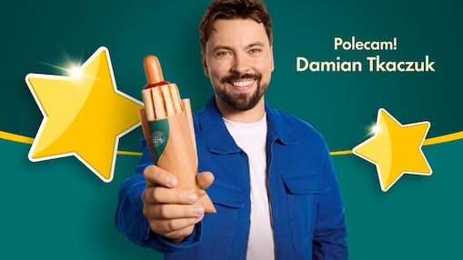 Na grafice widoczny jest influencer Damian Tkaczuktrzymający hot doga shell cafe, oraz podpis polecam, Damian Tkaczuk.